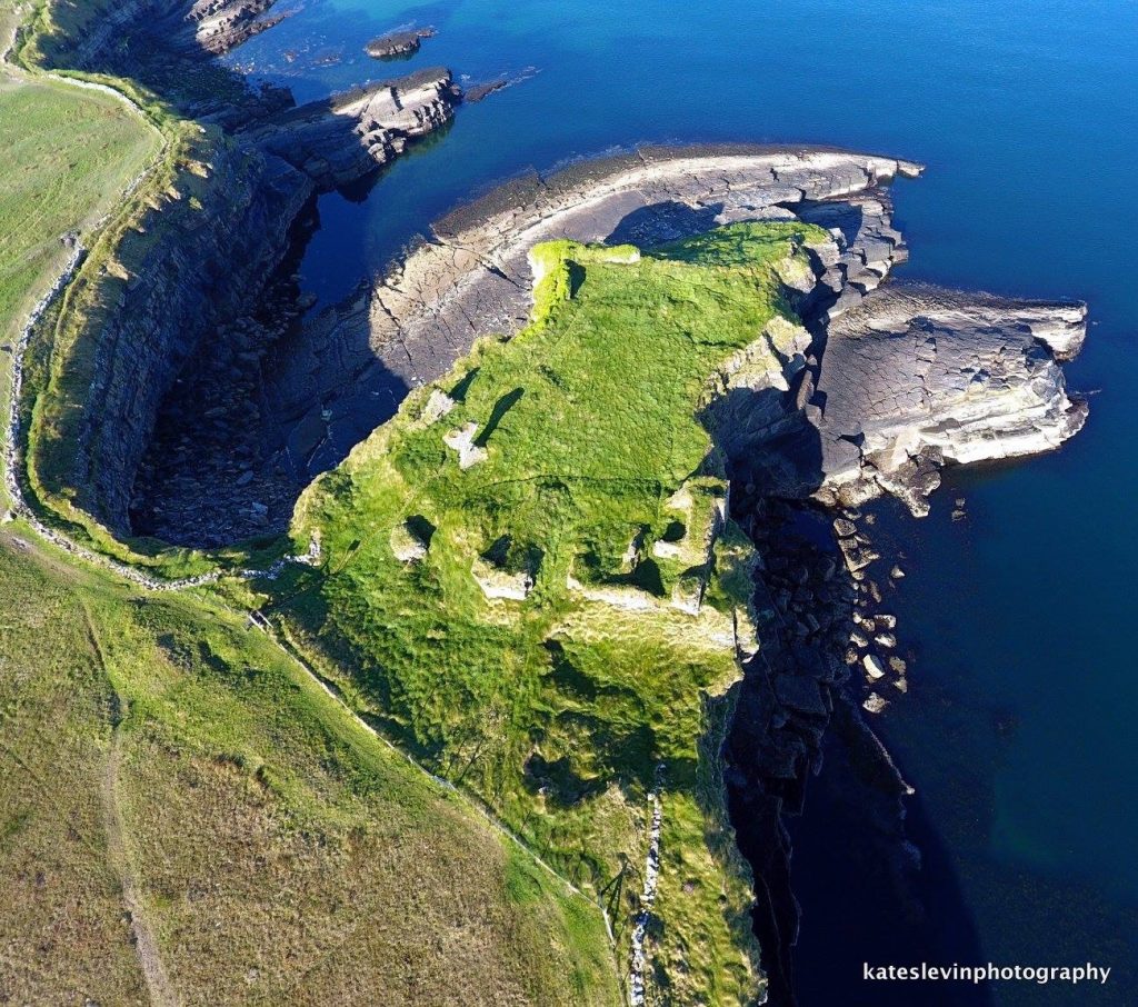An aerial view of the ruins of Kilbarron Castle perched at the top of the cliffs of the promontory jutting out into Donegal Bay. 